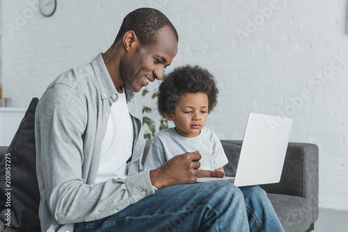 side view of african american father watching something at laptop with son at home