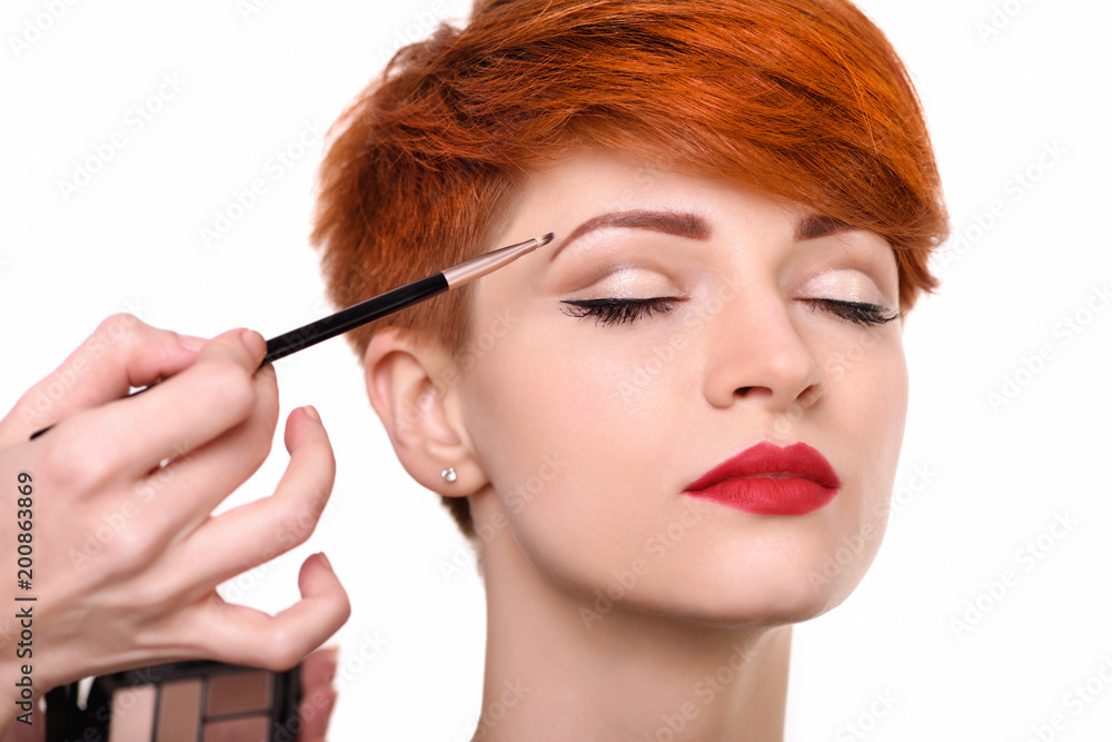 The artist is applying eyeshadow on her eyebrow with brush. The lady closed eyes with relaxation The artist is applying eyeshadow on her eyebrow with brush. The lady closed eyes with relaxation