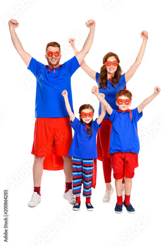 happy super family in costumes raising hands and smiling at camera isolated on white