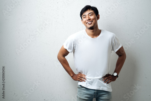 Young asian guy in white blank t-shirt, grunge wall, studio portrait