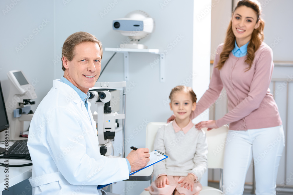 smiling mother, daughter and ophthalmologist looking at camera in oculist consulting room smiling mother, daughter and ophthalmologist looking at camera in oculist consulting room