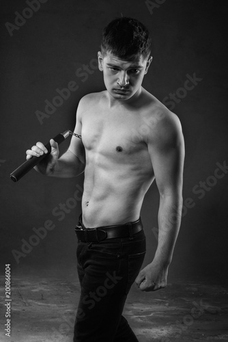 The muscled man on a black background in  fighting pose with nunchak photo