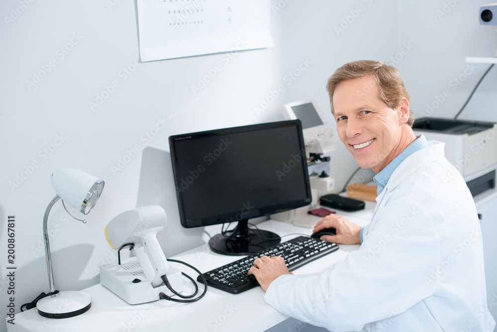 smiling male optician working with computer in clinic