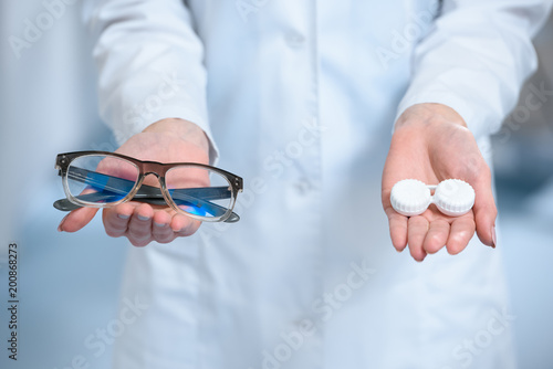 cropped view of ophthalmologist holding eyeglasses and and contact lenses in hands