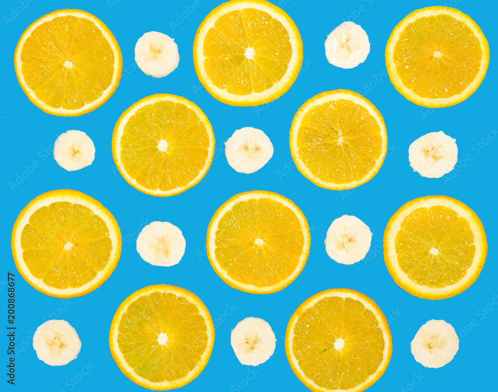 Colorful food fruit pattern of fresh orange and banana slices on bright blue background, top view, color wallpaper