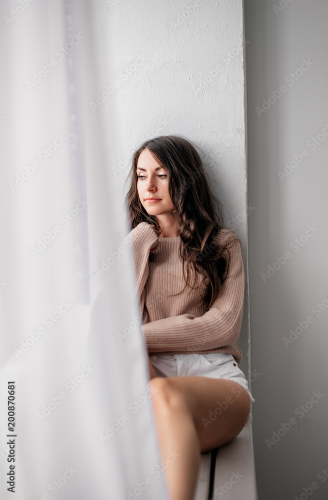 beautiful young brunette girl in white short shorts sitting on a windowsill beautiful young brunette girl in white short shorts sitting on a windowsill