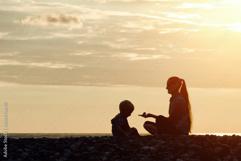 Mom and son playing on the beach with stones. Sunset time, silhouettes