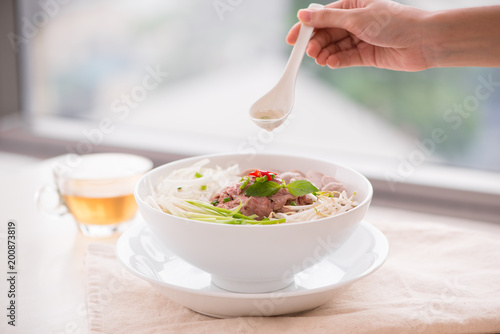Woman eating traditional Vietnamese Pho noodle using chopsticks.