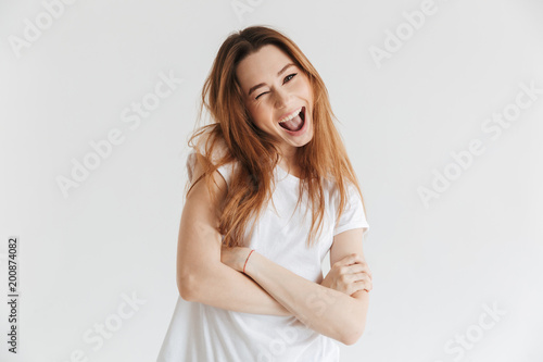 Cheerful woman in t-shirt with crossed arms winks her eye