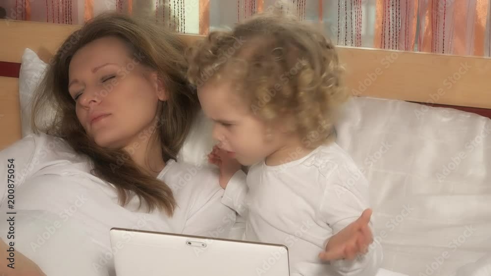 nice child girl looking at tablet computer while mother sleeping in bed nice child girl looking at tablet computer while mother sleeping in bed