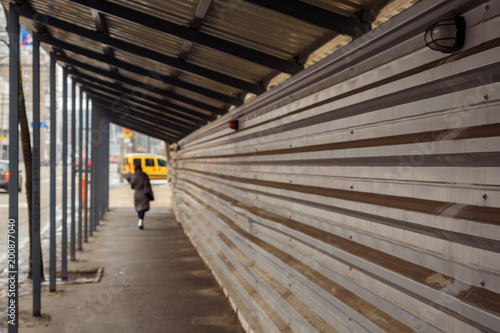 The girl walks under protective canopy over the sidewalk near a house under construction. Abstract: safety