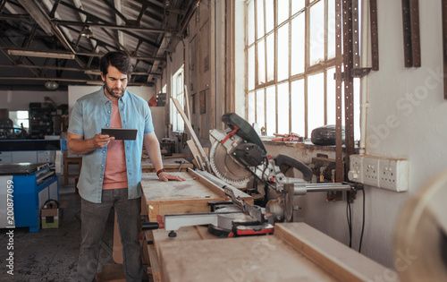 Young woodworker using a tablet in his carpentry workshop