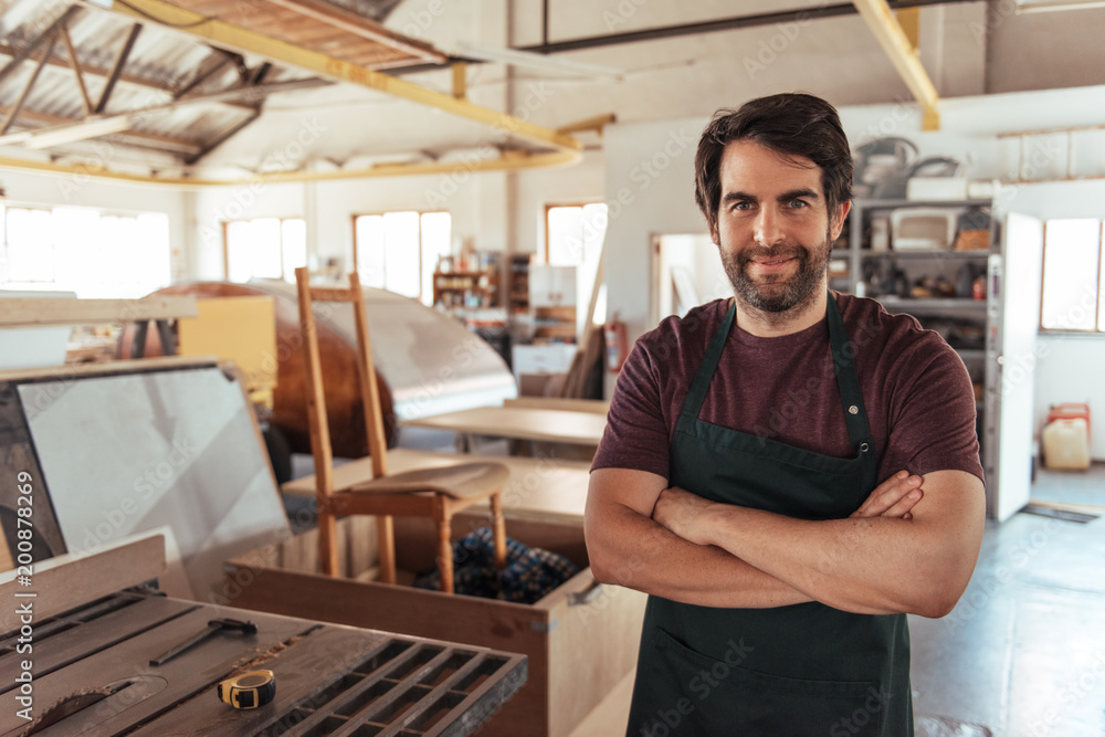 Smiling woodworker standing by a bench saw in his workshop Smiling woodworker standing by a bench saw in his workshop