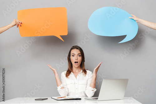 Photography Shocked young business woman using laptop computer near speech bubbles