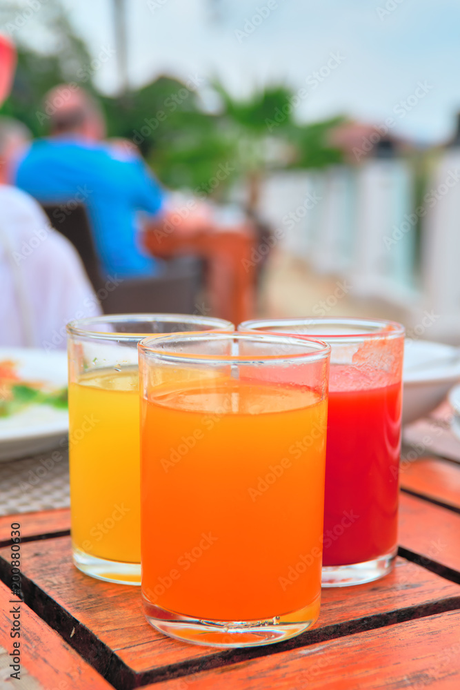 Three glasses with freshly squeezed juices: tomato, mango, orange stands on an vintage wooden table. Three glasses with freshly squeezed juices: tomato, mango, orange stands on an vintage wooden table.