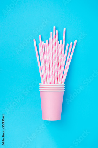 Stacked Drinking Paper Cups with Striped Straws on Mint Blue Background. Flat Lay Composition. Birthday Party Celebration Kids Fun. Cheerful Atmosphere. Greeting Card Poster Template. Copy Space