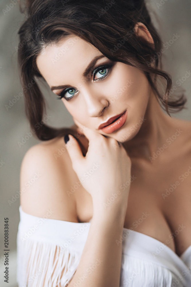 Portrait of beautiful attractive sexy woman in white with dark hair, blue eyes and sensual red lips standing in white dress with deep neckline opening her brest Portrait of beautiful attractive sexy woman in white with dark hair, blue eyes and sensual red lips standing in white dress with deep neckline opening her brest