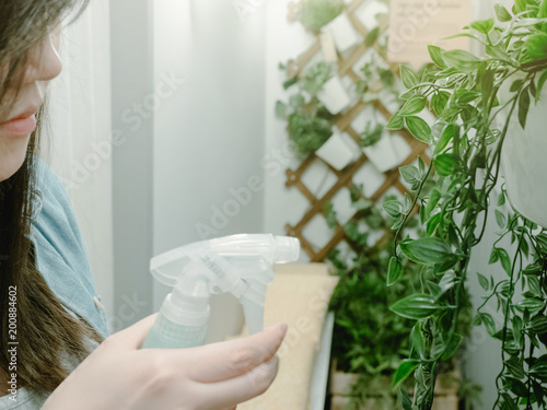 black hair asian hipster girl (25s to 35s) with blue jacket jean during relax spray or watering to small tree with soft focus decoratation background photo