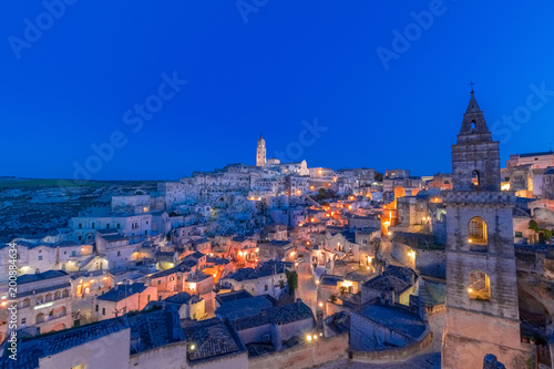 panoramic view of typical stones Sassi di Matera and church of Matera under blue night sky. Basilicata, Italy with clouds movement in the sky