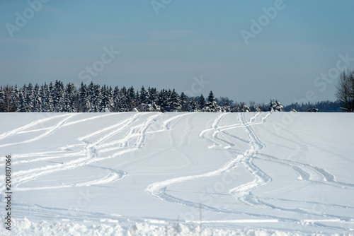 Drawings from snowmobile tracks on a snow-covered field in a winter day