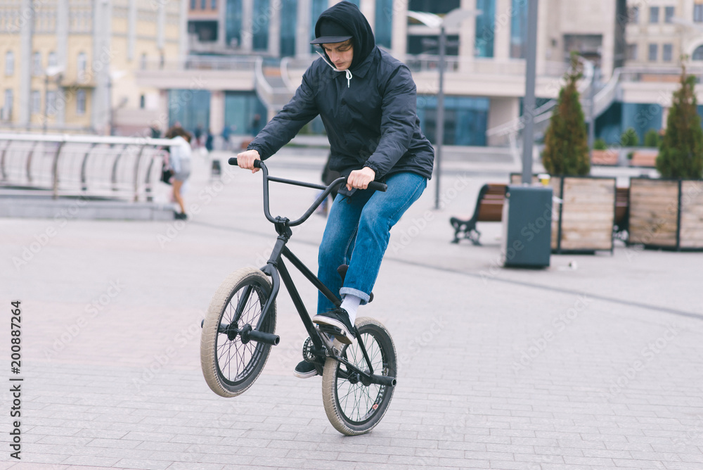 The teen does tricks on the BMX. BMX cyclist rides a bike around the park and makes tricks. BMX concept