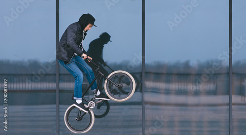 BMX freestyle. Stylish man doing tricks on BMX against a dark shop window. Street culture