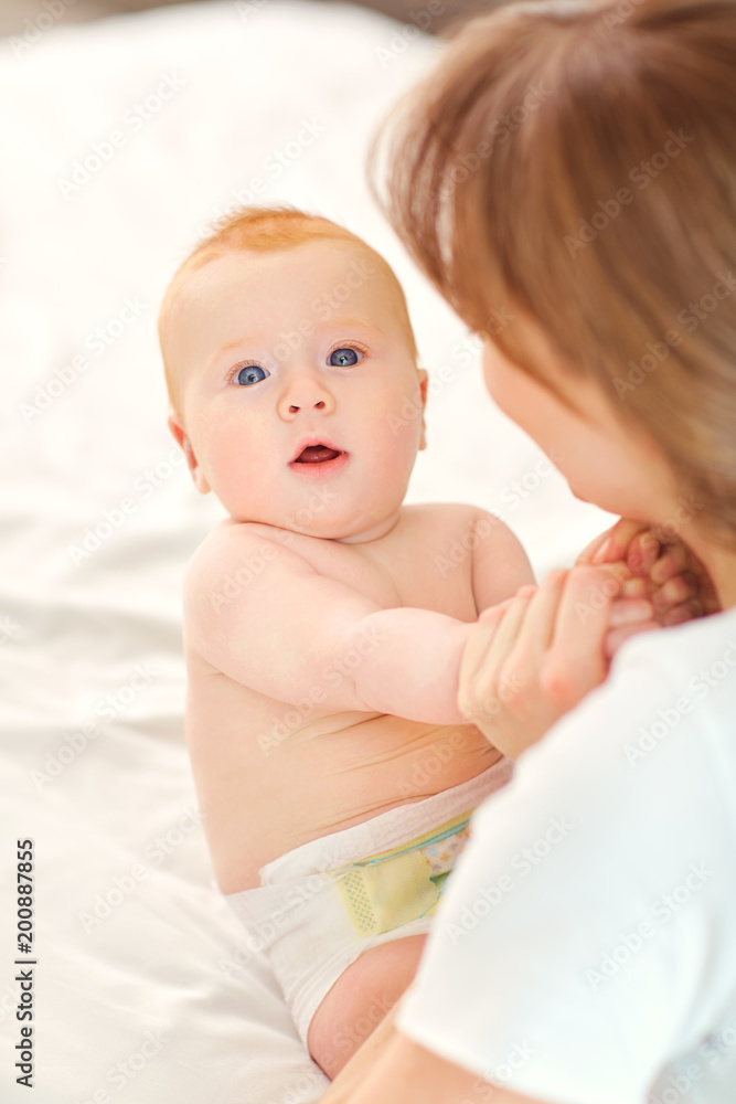 Happy mother with baby sitting on the bed indoors. Mothers day. Happy mother with baby sitting on the bed indoors. Mothers day.