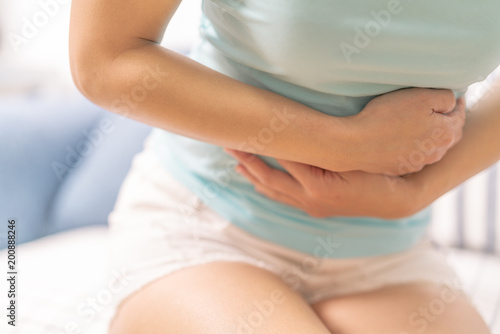 Young woman suffering from abdominal pain while sitting on the sofa and feeling stomachache, symptom of pms photo