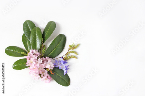 Spring botanical floral composition. Dcorative corner. Pink Japanese cherry blossoms, blue scilla flowers and evergreen English laurel branch isolated on white wooden background. Styled stock photo