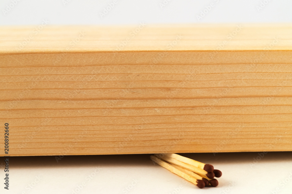 A few matches, laid in a bundle, crushed by a thick wooden board on a white background.