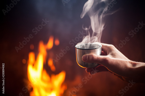 Hand holding cup of hot tea by the fire photo