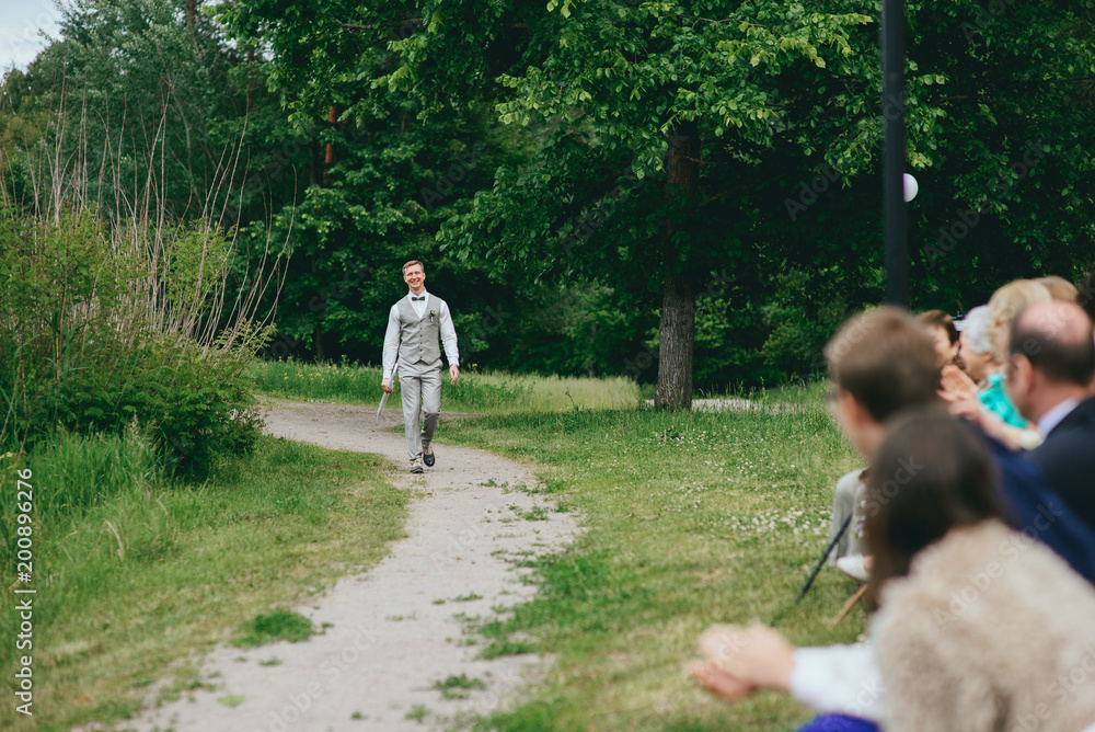 Fototapeta premium Groom in the stylish wedding suit going to the bride with a bouquet of flowers. Back view