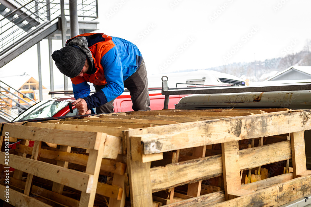 Man is loading wooden pallets on a truck in winter. Stacking wooden euro pallets on a truck lorry container for shipping and transport. Man is loading wooden pallets on a truck in winter. Stacking wooden euro pallets on a truck lorry container for shipping and transport.