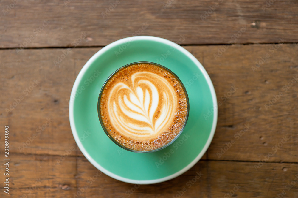 Top view of a cup of piccolo latte hot coffee on a green saucer with latte art and on wooden table background.