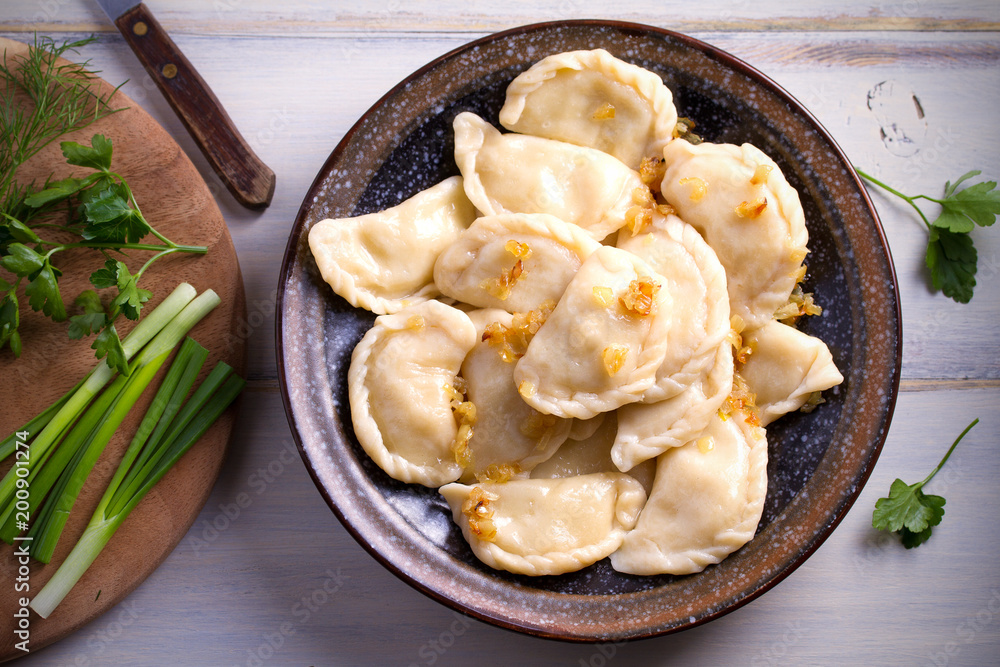 Pierogi or pyrohy, varenyky, vareniki, dumplings served with caramelized salted onion in bowl on wooden table. horizontal
