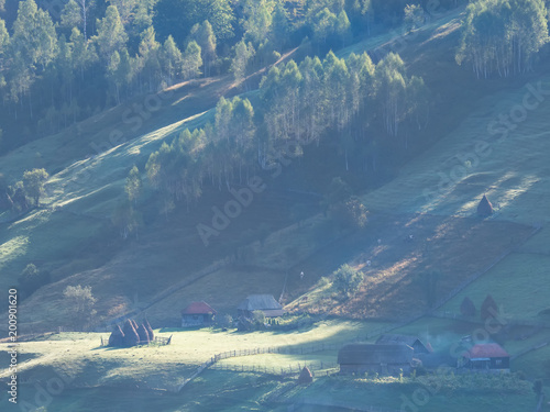 Beautiful rural mountain landscape in the morning light with fog,old houses and haystacks, Fundatura Ponorului, Hunedoara County, Romania photo