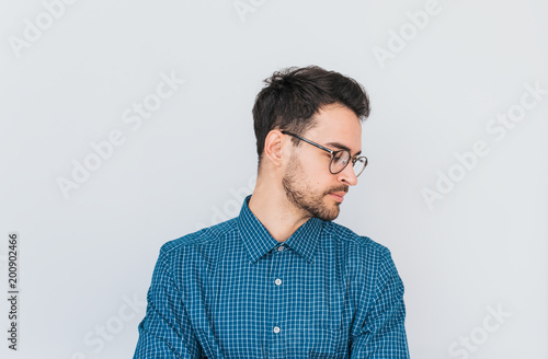 Closeup horizontal portrait of handsome male model in glasses and blue shirt, looking down posing against white studio wall background. People and business concept. Copy space for your advertisement.