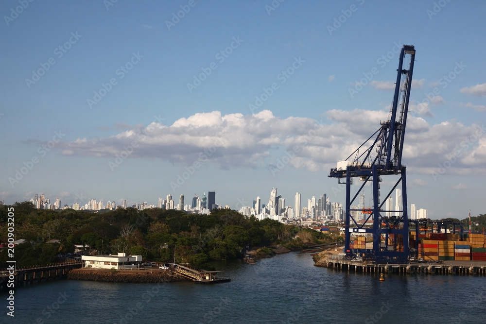 Cargo port with crane & shipping containers along the entrance to the Panama Canal, with Panama city in the background.