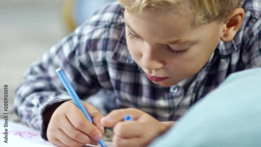 Close up shot of smart schoolboy lying on the floor and drawing picture with blue felt-tip pen Close up shot of smart schoolboy lying on the floor and drawing picture with blue felt-tip pen