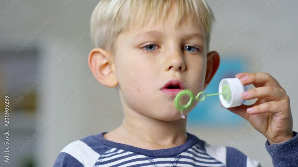 Close up face of adorable boy of primary school age using bubble wand to blow soap bubbles Close up face of adorable boy of primary school age using bubble wand to blow soap bubbles
