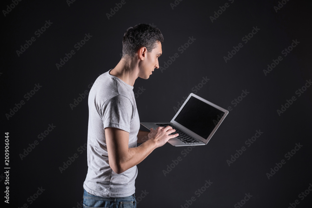Modern device. Smart nice confident man holing a laptop and looking at its screen while using it for work Modern device. Smart nice confident man holing a laptop and looking at its screen while using it for work