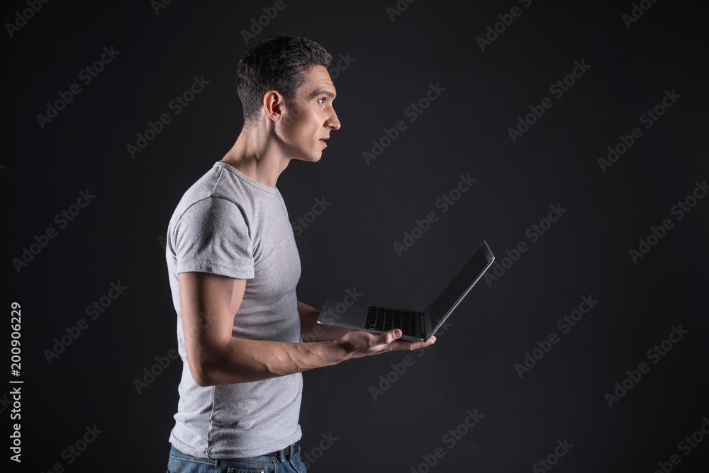 Smart technology. Confident nice excited man holding his laptop and starring at the laptop screen while using smart technology Smart technology. Confident nice excited man holding his laptop and starring at the laptop screen while using smart technology