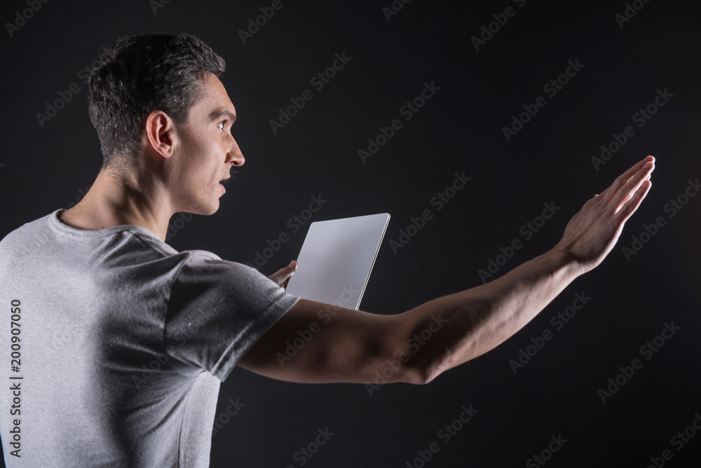 Progressive technology. Intelligent nice brunette man holding a tablet and stretching out his hand while working with a computer sensory panel Progressive technology. Intelligent nice brunette man holding a tablet and stretching out his hand while working with a computer sensory panel