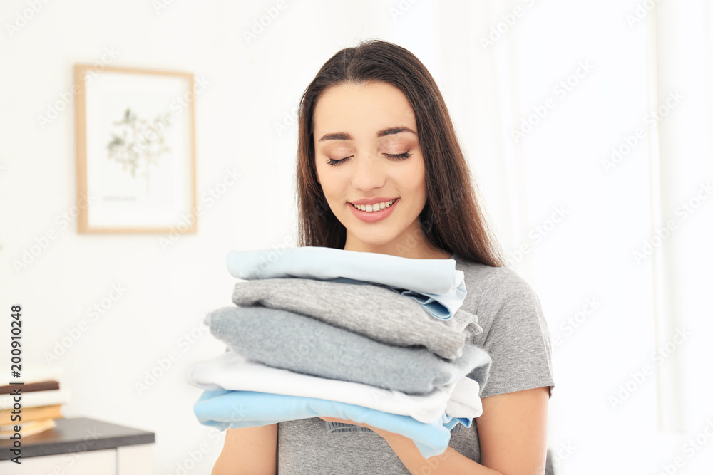 Woman holding stack of clean clothes indoors. Laundry day Woman holding stack of clean clothes indoors. Laundry day