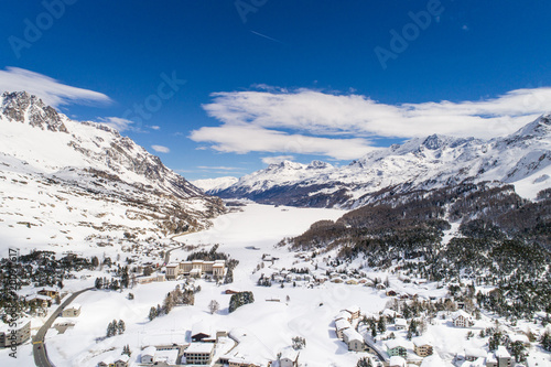 Valley of Engadine in winter season, aerial view. Village of Maloja and alpine lake covered with snow