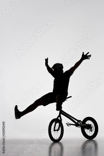silhouette of trial biker sitting on handlebars of bicycle on white
