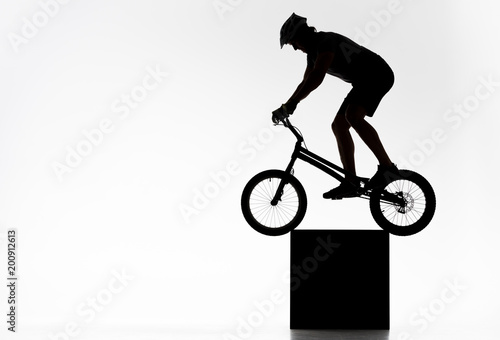 silhouette of trial cyclist balancing on cube on white