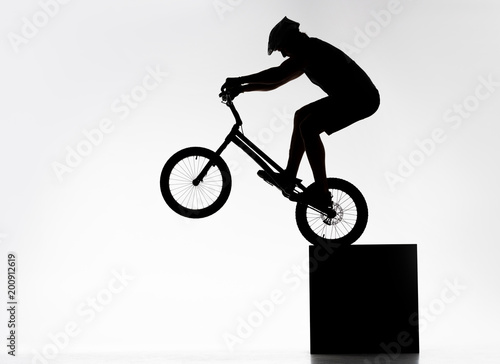 silhouette of trial cyclist performing back wheel stand while balancing on cube on white