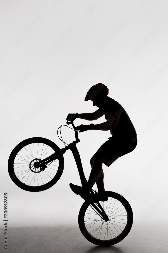 Naklejka premium silhouette of trial biker standing on back wheel on white