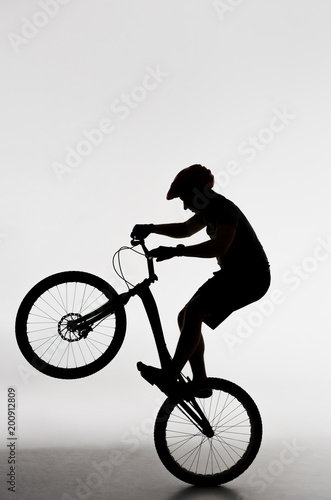 silhouette of trial biker standing on back wheel on white